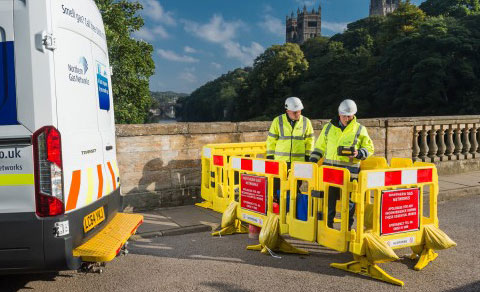 Two workmen surrounded by safety barriers. The back of a Northern Gas Networks van is on their left.